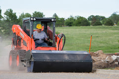 Kubota SSV75 skid steer with pickup broom sweeper cleaning a jobsite road