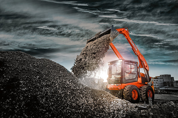 Kubota SSV75 skid steer with bucket dumping gravel on a stockpile