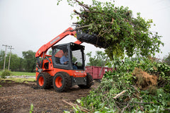 Kubota SSV75 skid steer loader with root grapple lifting brush on a land clearing job