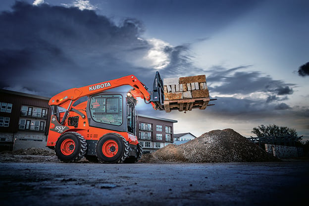 Kubota SSV75 skid steer with pallet forks lifting a pallet of pavers
