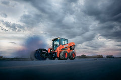 Kubota SSV75 skid steer with sweeper attachment on an open lot